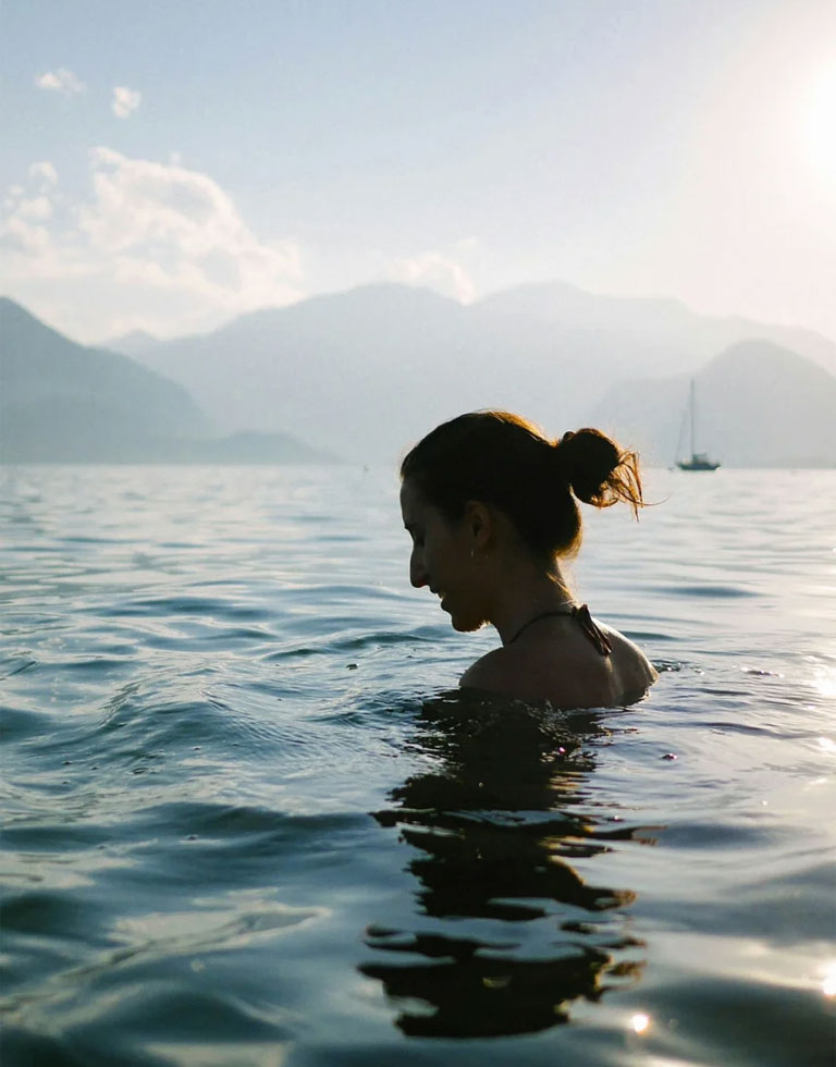 A woman in open water, mountains and a boat behind her